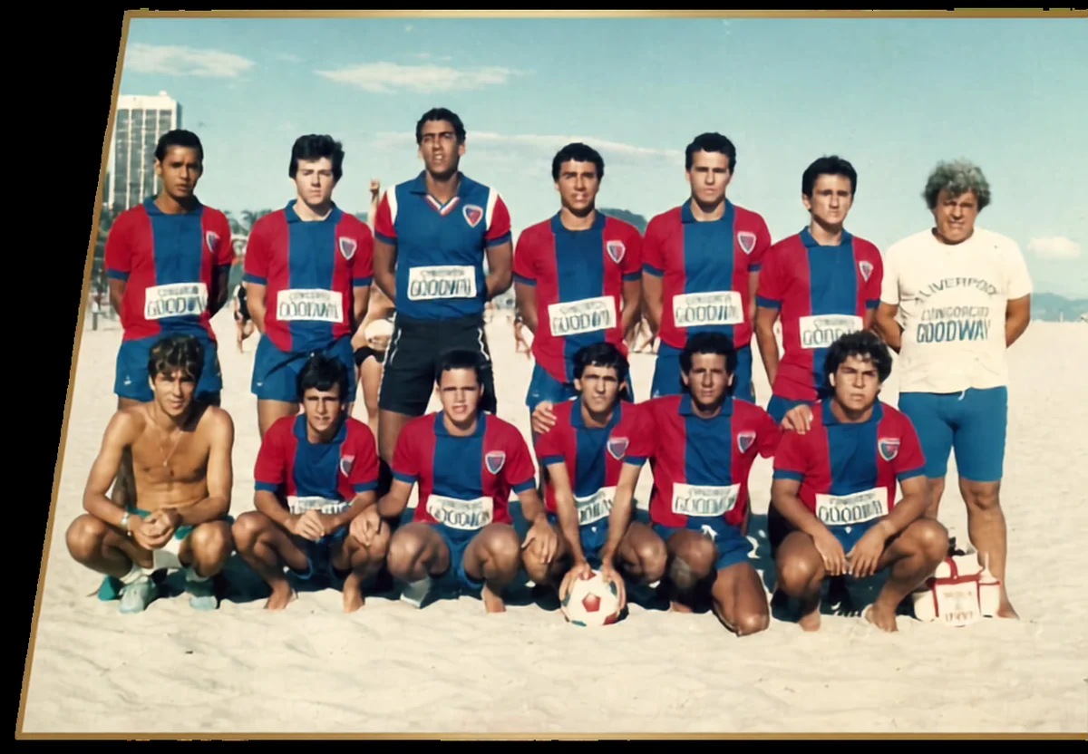 Jogadores em uniformes azuis e vermelhos e outras pessoas reunidos na areia.