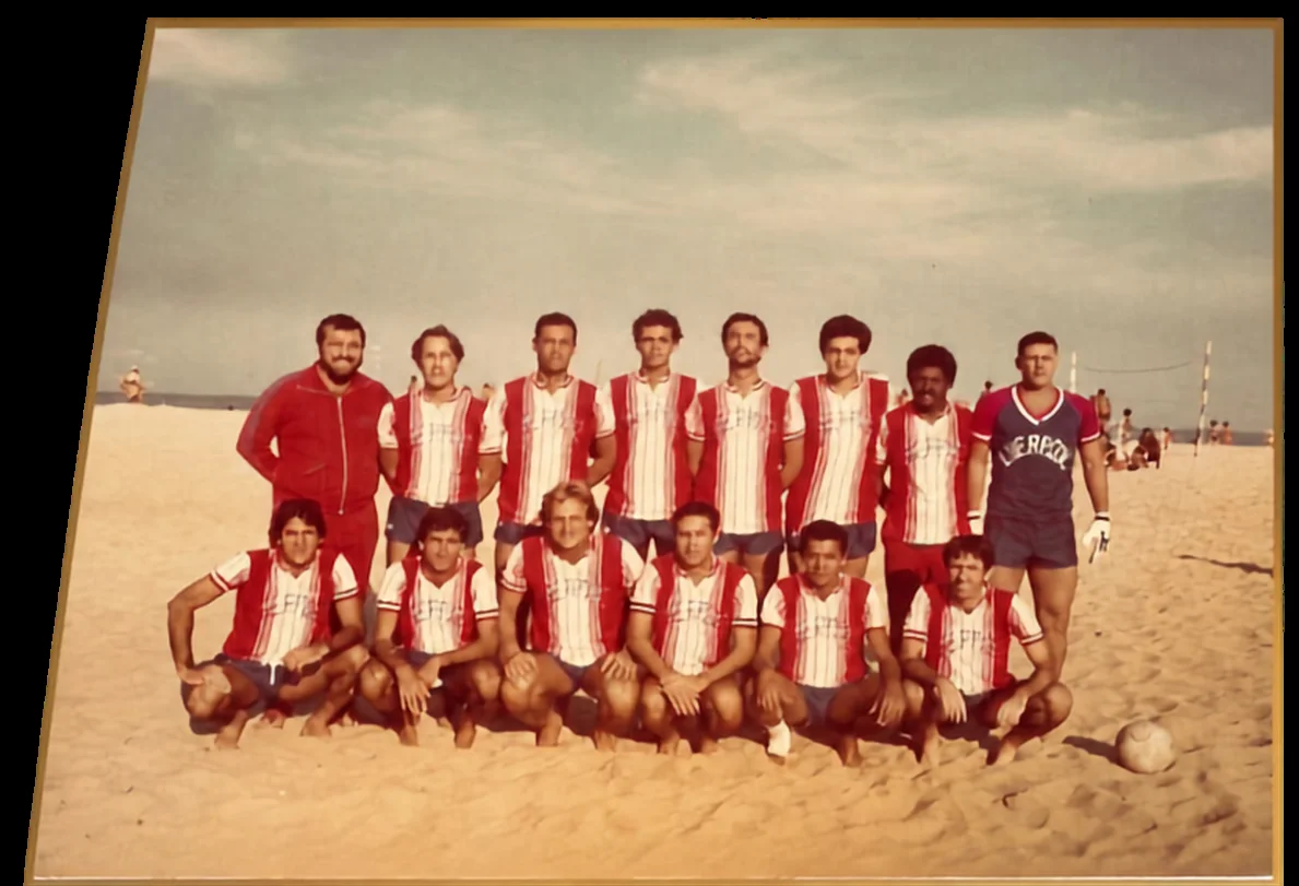 Equipe com camisas listradas em vermelho e branco reunida na praia.